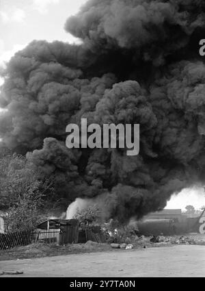 UNE DÉCHARGE EN CAOUTCHOUC BRÛLE À NEW MALDEN 22 mai 1950 des nuages de fumée noire ont couvert New Malden, Surrey, aujourd'hui (lundi) lorsqu'une décharge en caoutchouc a pris feu sur St Johns Road. Les pompiers de Surrey combattant l'incendie ont déclaré que la décharge était «bien allumée» des images montrent : des nuages denses de fumée roulant au-dessus de la décharge flamboyante aujourd'hui. Banque D'Images