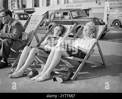 Chaussures off à Brighton - journée la plus chaude de l'année à BrightonBrighton a enregistré la journée la plus chaude de l'année avec une température de 80 degrés . De grandes foules affluaient vers la côte et les plages de Brighton étaient remplies par des vacanciers tardifs profitant de la vague de chaleur inattendue de l'automne. Photos : deux visiteurs londoniens Shirley O'Sullivan (à gauche) et Vicki Forrest (à droite) enlèvent leurs chaussures et font une sieste sous le soleil brillant sur la promenade de Brighton , West Sussex 29 septembre 1946 Banque D'Images