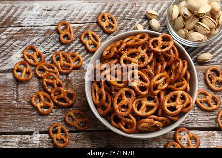 Délicieux craquelins de bretzel salés et pistaches sur table en bois, pose à plat Banque D'Images