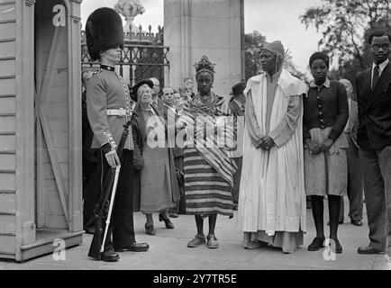 L'uniforme écarlate et la peau d'ours portés par une sentinelle en service à l'extérieur du palais de Buckingham, sont admirés par le roi habillé Akenzua II, Oba du Bénin, sa femme, la reine Ohan et leur fille de 19 ans, la princesse Egbebakhame (à droite), Londres, Angleterre. - - L'Oba, dirigeant de 1 000 000 Nigérians, est arrivé en Angleterre hier en tant qu'invité du British Council. Avec lui, il apporta un message de bonne volonté au roi. - - 12 août 1950 Banque D'Images