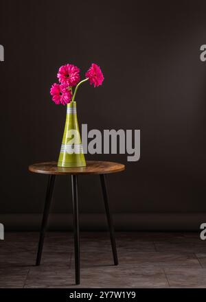 Trois fleurs lumineuses dans un grand vase léger se tiennent sur une table ronde, attirant l'attention avec leur coloration juteuse. L'arrière-plan sombre accentue le contraste. Banque D'Images