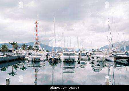 Catamarans blancs se tiennent dans une rangée avec des yachts à moteur et à voile à l'embarcadère avec une grue portuaire Banque D'Images