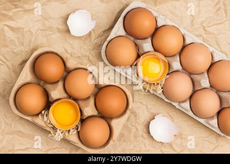 Faire dorer les œufs de poule dans un récipient en carton. Oeuf cassé dans le récipient. Coquille d'oeuf sur table. Fond brun de papier froissé. Pose à plat Banque D'Images