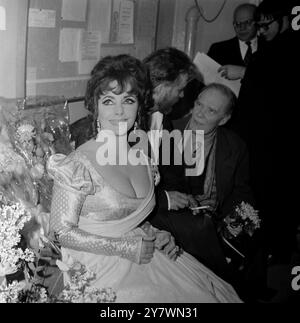 N'ayant pas dit un mot tout au long de la performance ... actrice Elizabeth Taylor est assis silencieusement dans le vestiaire comme mari Richard Burton parle à la presse ... après l'ouverture de la nuit du Docteur Faustus à l'Oxford Playhouse . Les deux stars ont donné leurs services gratuitement pour la semaine de cette pièce , dont les profits sont en aide à la Oxford University Dramatic Society . 15 février 1966 Banque D'Images