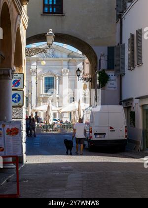 Mantoue, Italie 30 septembre 2024 Un homme avec son chien marche sous une arche dans le centre historique de mantoue, italie, menant à une place avec outdoo Banque D'Images