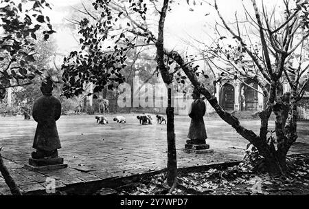 Gardé par des statues de mandarins , d'éléphants , de bétail et de chevaux : un mausolée oriental des empereurs morts . Où les morts royaux sont enterrés dans la terre sans linceul ni cercueil , à un endroit non marqué dans une vaste enceinte : des dévots annamites s'inclinant devant le Pavillon de la mémoire , dans la cour d'honneur du tombeau de Minh Mang l'Erudite . Près de Hue , la capitale de l'Annam. 14 mars 1925 Banque D'Images