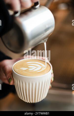Mains féminines versant du lait et préparant un cappuccino frais. Artiste de café. Vue latérale. Café-restaurant. Banque D'Images