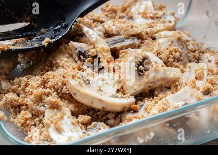 Champignons tranchés mélangés avec de la chapelure complète dans un plat en verre. Concept de préparation des aliments. Banque D'Images