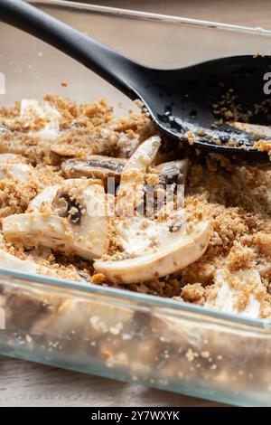 Champignons tranchés mélangés avec de la chapelure complète dans un plat en verre. Concept de préparation des aliments. Banque D'Images