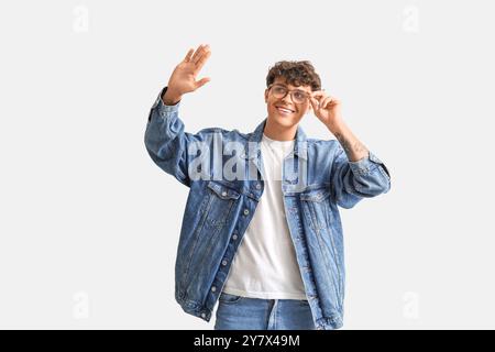 Jeune homme dans des lunettes élégantes agitant la main sur fond clair Banque D'Images