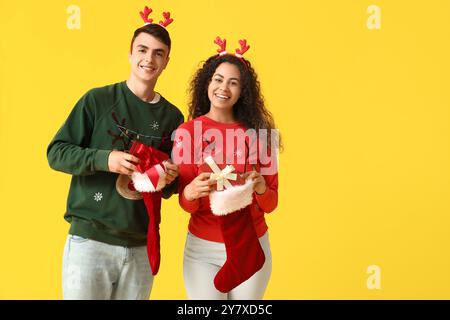 Heureux jeune couple en pulls avec des chaussettes de Noël et des boîtes cadeaux sur fond jaune Banque D'Images