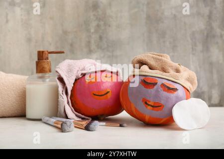 Citrouilles drôles avec des masques faciaux, des pinceaux de maquillage et un produit cosmétique sur la table sur fond grunge Banque D'Images