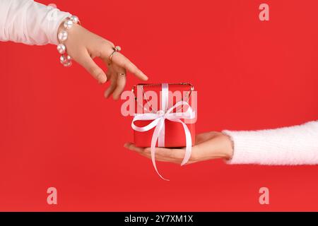 Mains féminines avec boîte cadeau de Noël et bijoux élégants sur fond rouge Banque D'Images