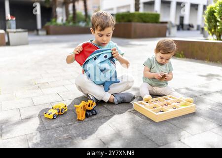 Deux frères caucasiens assis sur le sol et jouant avec des jouets dans le parc Banque D'Images