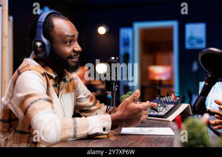 Un gars afro-américain parle dans le microphone tout en menant une émission de radio en ligne. Un épisode de podcast mettant en vedette un animateur d'homme noir faisant une interview dans son home studio pour un public internet. Banque D'Images