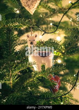 Un charmant lama en feutre fait à la main est accroché à une branche de sapin de Noël, entouré de lumières scintillantes de vacances. La scène confortable capture la chaleur o Banque D'Images