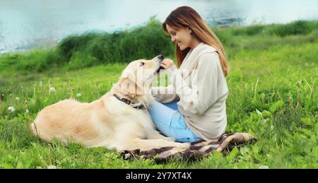 Heureux propriétaire jeune femme nourrissant son chien Golden Retriever sur l'herbe ensemble dans le parc d'été Banque D'Images