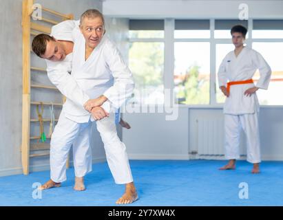 Cours de judo ou de jiu-jitsu - deux hommes d'âge différent pratiquant la saisie et le lancer sur des tapis de sport Banque D'Images