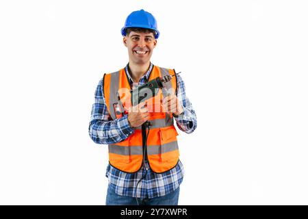 travailleur de la construction dans un gilet réfléchissant orange et casque de sécurité sourit tout en tenant une perceuse, prêt pour le travail sur un chantier de construction. Le port d'image Banque D'Images