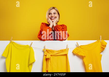 Belle jeune femme souriant sur les vêtements colorés accrochés à la corde à linge Banque D'Images