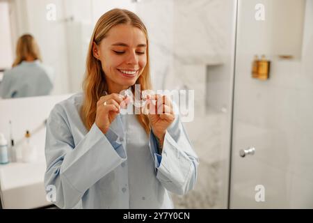 Une femme souriante avec des aligneurs clairs dans un cadre de salle de bain élégant, moderne et contemporain Banque D'Images