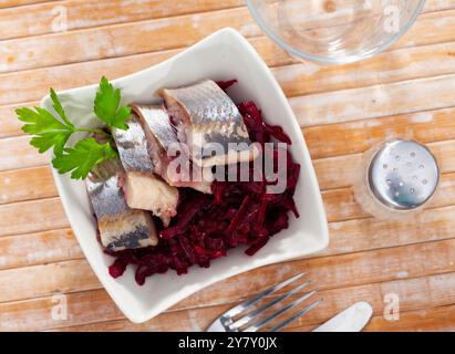 Salade de hareng appétissante avec betteraves, crème sure et persil dans une assiette blanche Banque D'Images