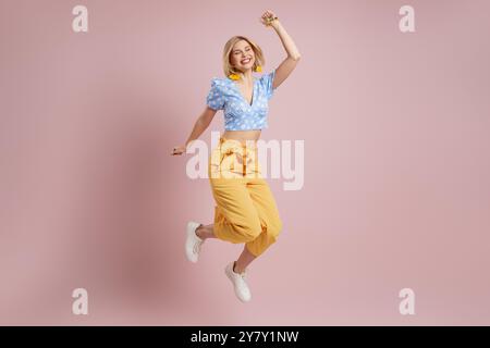 Pleine longueur de jeune femme excitée sautant et souriant sur fond rose Banque D'Images