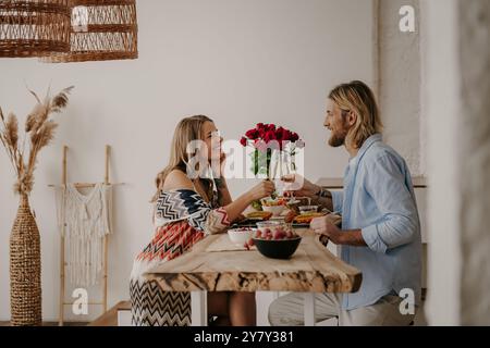 Joyeux jeune couple aimant toast avec champagne tout en ayant un dîner romantique à la maison de style boho Banque D'Images