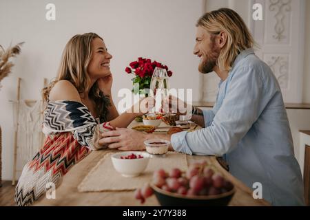 Joyeux jeune couple aimant toast avec champagne tout en célébrant l'anniversaire à la table à la maison Banque D'Images