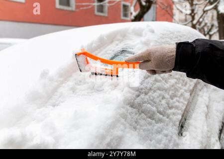 Conduite en hiver. Gros plan d'une main nettoyant le pare-brise d'un véhicule de la glace et de la neige. Transport, hiver, météo, personnes et véhicule conce Banque D'Images