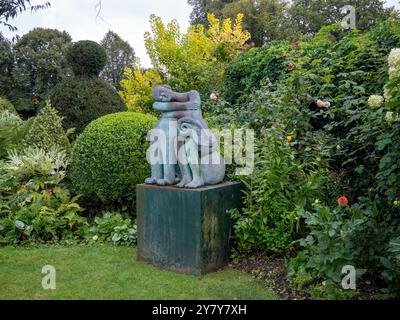 Chenies Manor Garden en septembre ; coin du jardin avec des feuilles persistantes, arbustes, topiaire et une sculpture d'une figure endormie et bélier. Banque D'Images