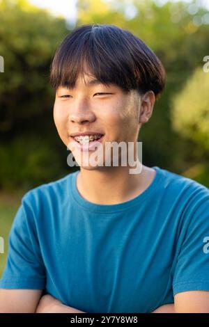 Adolescent asiatique souriant avec des bretelles portant une chemise bleue à l'extérieur dans le jardin Banque D'Images