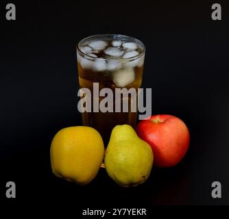 Un grand verre d'un mélange de jus de fruits avec de la glace sur un fond noir, à côté de pommes mûres et de poires. Gros plan. Banque D'Images