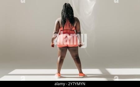 Vue arrière pleine longueur de la femme africaine de taille plus dans les vêtements de sport debout dans le studio de fitness Banque D'Images