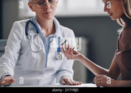 Jeune femme examinant le flacon avec le médicament pendant la visite de soins de santé en clinique Banque D'Images