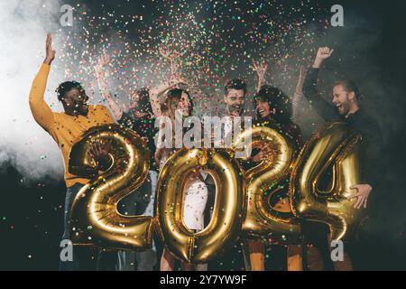 Groupe de jeunes heureux célébrant le nouvel an 2024 tout en jetant des confettis dans la boîte de nuit Banque D'Images