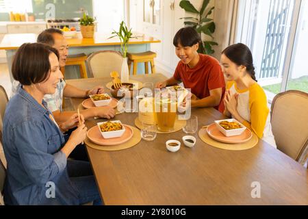 Famille multiraciale appréciant le repas ensemble à la table à manger, souriant et parlant heureux Banque D'Images