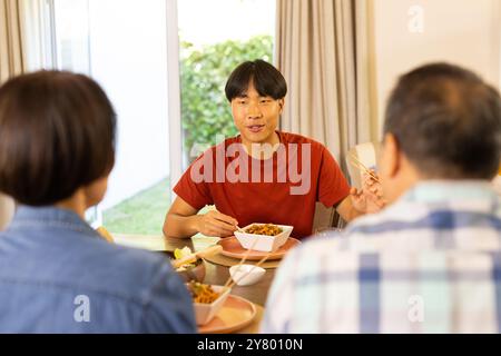À la maison, manger le dîner, la famille asiatique profitant de repas ensemble à la table à manger, souriant et parlant Banque D'Images