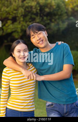 Souriant jeune frère asiatique et soeur embrassant et posant ensemble à l'extérieur dans le jardin Banque D'Images