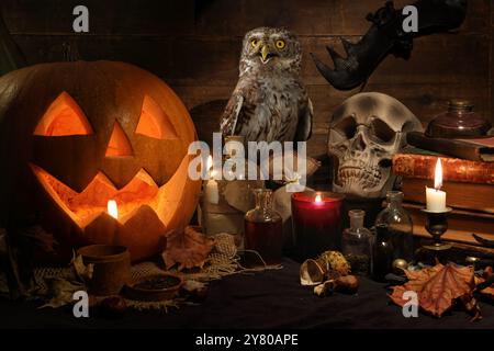 Vie morte effrayante avec crâne, citrouille, vieux livres, feuilles d'érable, bouteilles vintage, des bougies et un hibou eurasien assis sur une table de sorcière. Halloween o Banque D'Images