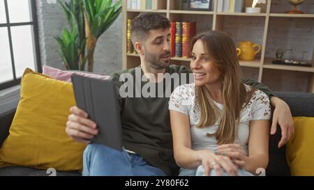 Un couple heureux s'engage dans un appel vidéo depuis leur salon confortable, mettant en valeur leur relation et l'intérieur moderne de la maison. Banque D'Images