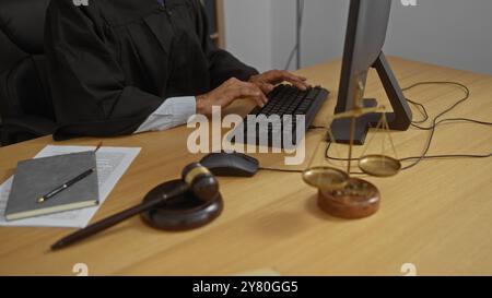 Homme tapant sur un clavier dans une salle d'audience, entouré par le marteau du juge, l'échelle de la justice, des documents juridiques, et le bloc-notes, représentant un juridique sérieux Banque D'Images