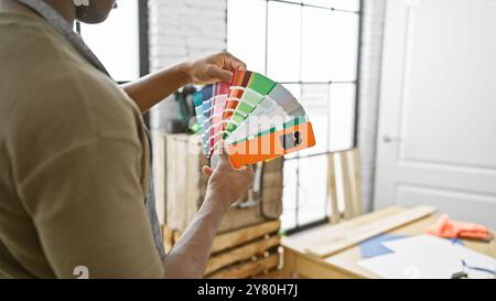 Homme afro-américain examinant des échantillons de couleur dans un atelier de menuiserie lumineux. Banque D'Images