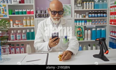 Homme dans la pharmacie tenant smartphone et bouteille de médicament tout en portant des lunettes et manteau blanc à l'intérieur de la pharmacie magasin avec des étagères de produits dans le BA Banque D'Images