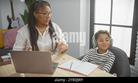 Une femme enseigne à un garçon portant des écouteurs à un ordinateur portable dans un salon, illustrant l'éducation familiale et l'école à domicile. Banque D'Images