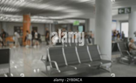 Vue défocalisée d'une zone de sièges de l'aéroport avec des voyageurs flous en arrière-plan ainsi que quelques sièges vides Banque D'Images