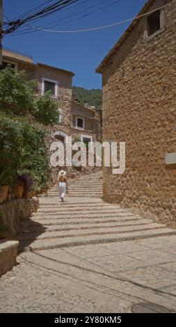 Femme marchant sur des marches de pierre bordées de plantes en pot dans le charmant village de fornalutx, majorque, espagne, sous un ciel bleu clair Banque D'Images