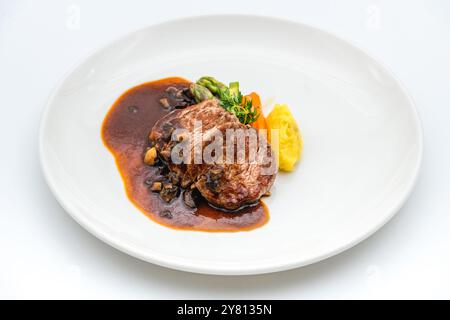 Filet de bœuf grillé avec sauce demi-glace et légumes grillés sur une assiette en porcelaine blanche Banque D'Images