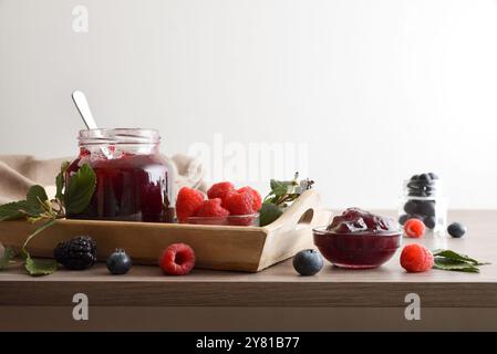 Confiture de fruits de la forêt sur un plateau en bois sur une table pleine de fruits avec fond blanc isolé. Vue de face. Banque D'Images