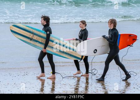 Trois surfeurs portant leurs planches de surf marchant le long du rivage sur la plage de Fistral à Newquay en Cornouailles au Royaume-Uni. Banque D'Images